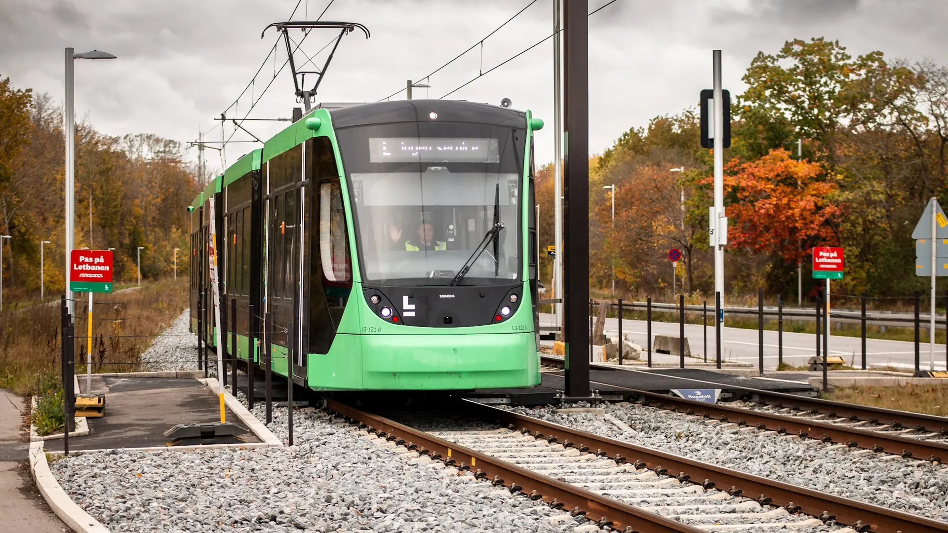 Fodgænger krydser letbanespor ved Z-krydsning i Ejby mens letbanetog nærmer sig med 70 km/t