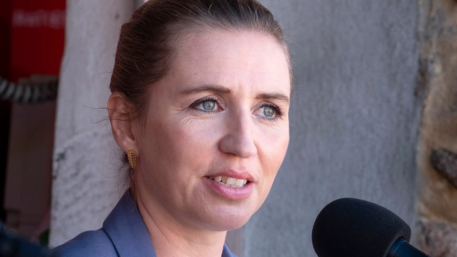 Ung kvinde sidder alvorligt foran en neutral baggrund, symboliserende de psykiske ar efter vold og flugt. Et billede på styrke, frygt og et system under pres. Hvad gør børnenes statsminister?